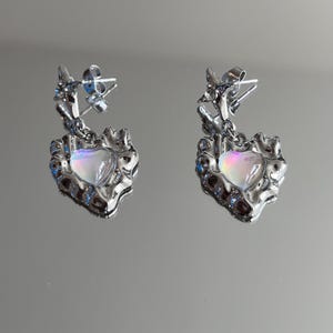 May include: A pair of silver earrings with a heart-shaped pendant featuring an iridescent, opalescent stone.