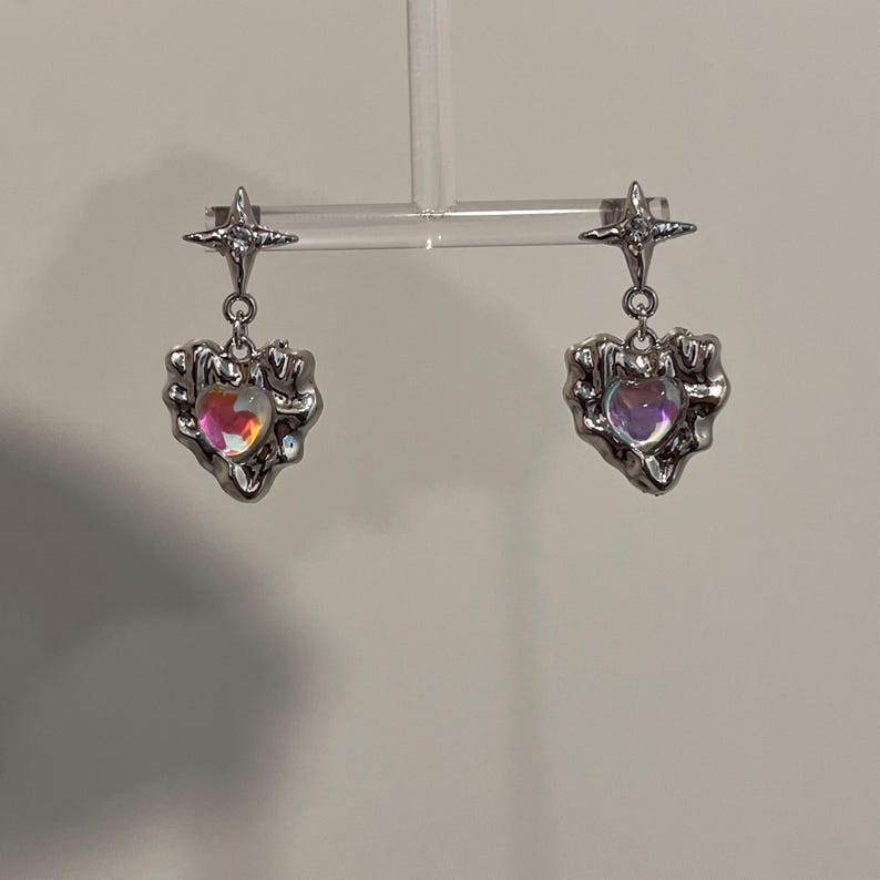 May include: A pair of silver earrings with a star charm and a heart-shaped pendant with an iridescent stone.
