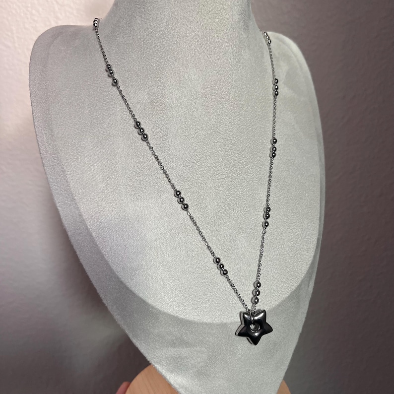 Peut inclure: Un collier en cha&icirc;ne argent&eacute;e avec un pendentif en forme d'&eacute;toile. L'&eacute;toile a un petit trou au centre.