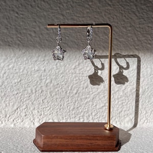 May include: A pair of silver star-shaped earrings with clear stones hanging from a gold stand.