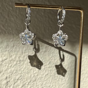 May include: A pair of silver hoop earrings with a dangling star charm. Each star is encrusted with clear cubic zirconia stones.