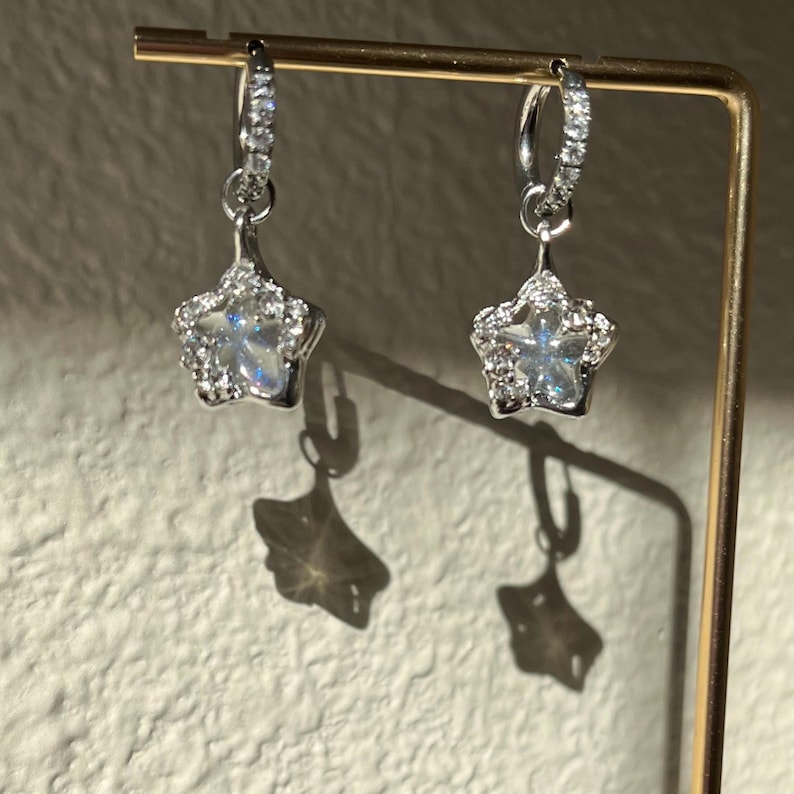 May include: A pair of silver hoop earrings with a dangling star charm. Each star is encrusted with clear cubic zirconia stones.