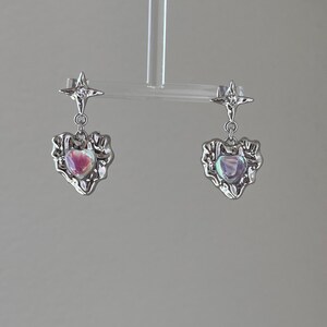 May include: A pair of silver earrings with a star charm and a heart-shaped pendant with an iridescent stone.