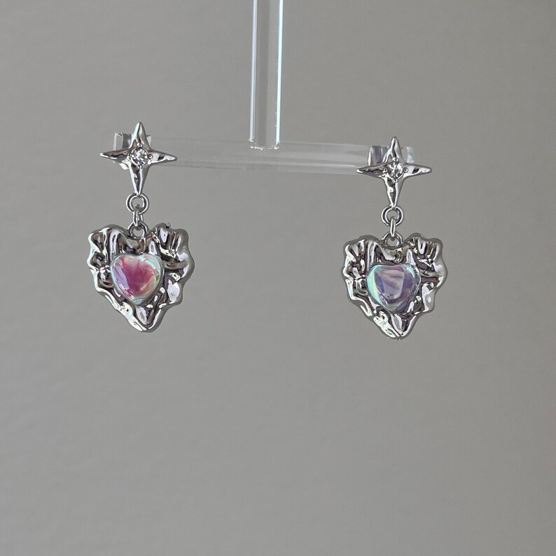 May include: A pair of silver earrings with a star charm and a heart-shaped pendant with an iridescent stone.