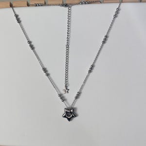 Peut inclure: Un collier en argent avec un pendentif en forme d'&eacute;toile. Le collier a une cha&icirc;ne avec de petites perles argent&eacute;es et un charme en forme d'&eacute;toile au bout de la cha&icirc;ne.