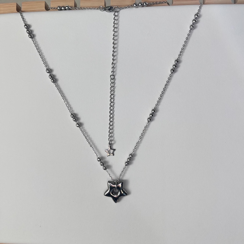 Peut inclure: Un collier en argent avec un pendentif en forme d'&eacute;toile. Le collier a une cha&icirc;ne avec de petites perles argent&eacute;es et un charme en forme d'&eacute;toile au bout de la cha&icirc;ne.