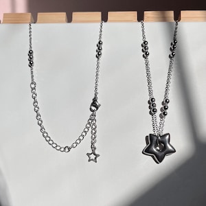 Peut inclure: Deux colliers en argent, l'un avec un pendentif en forme d'&eacute;toile et l'autre avec un pendentif en forme d'&eacute;toile plus grand avec un trou au centre.