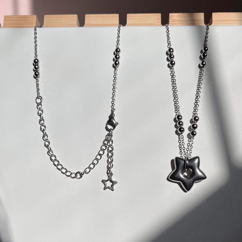 Peut inclure: Deux colliers en argent, l'un avec un pendentif en forme d'&eacute;toile et l'autre avec un pendentif en forme d'&eacute;toile plus grand avec un trou au centre.