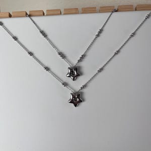 Peut inclure: Deux colliers en argent avec des pendentifs en forme d'&eacute;toile. Les colliers sont superpos&eacute;s sur un fond blanc.