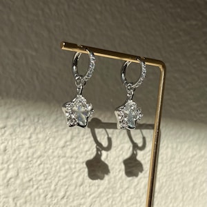 May include: A pair of silver hoop earrings with a dangling star charm. Each star charm is encrusted with clear cubic zirconia stones.