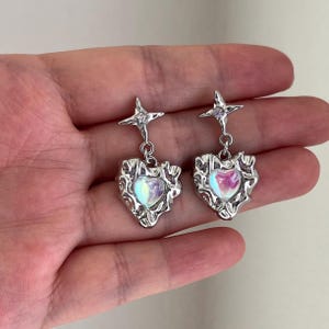 May include: A pair of silver earrings with a star charm and a heart-shaped pendant with an iridescent finish.