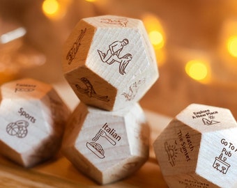 May include: Five wooden dice with different activities printed on each side. The dice are in a pyramid shape with the top die showing a couple dancing. The other dice show activities like "Go To A Pub", "Watch The Sunset", "Explore A New Place", "Italian", and "Sports".