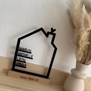 May include: A black house-shaped family sign with the names Marvin, Michelle, Leon, and Jonas. The sign sits on a wooden base with the text "Familie Winkler". A small heart is at the top of the house outline.