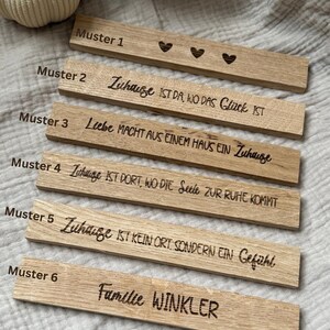 May include: Wooden rectangular plaques with engraved text and heart designs. The plaques feature phrases in German, such as "Zuhause ist da, wo das Gl&uuml;ck ist" and "Familie Winkler". The plaques are made of light-colored wood.