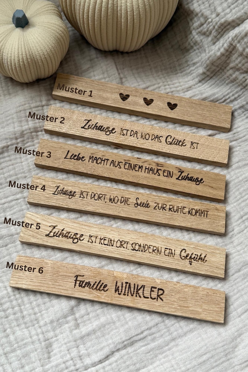 May include: Wooden rectangular plaques with engraved text and heart designs. The plaques feature phrases in German, such as "Zuhause ist da, wo das Gl&uuml;ck ist" and "Familie Winkler". The plaques are made of light-colored wood.