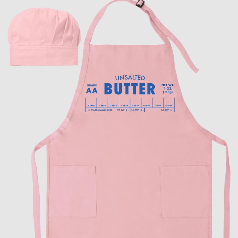 May include: A light pink apron and chef's hat set. The apron features the words "UNSALTED BUTTER" in blue, along with a measurement guide. The net weight is 4 oz (113g). The apron has two pockets and an adjustable neck strap.