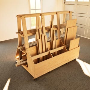 Op de afbeelding: Een houten opslagwagen voor hout met meerdere compartimenten en planken. De wagen is gemaakt van lichtgekleurd hout en is gevuld met hout en panelen van verschillende afmetingen. Hij heeft wielen voor gemakkelijke mobiliteit.