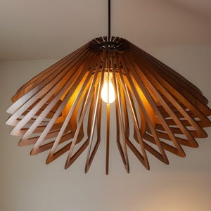 Puede incluir: Una lámpara colgante de madera con un diseño geométrico único. La lámpara está hecha de listones de madera delgados que están dispuestos en un patrón radial. La lámpara está iluminada por una sola bombilla.