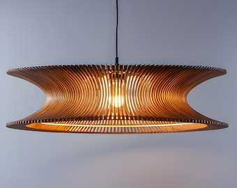 Peut inclure: Un luminaire suspendu en bois moderne avec un design incurvé unique. La lumière est faite de fines lattes de bois disposées en un motif circulaire. La lumière est suspendue à un cordon noir et possède une ampoule incandescente chaude.