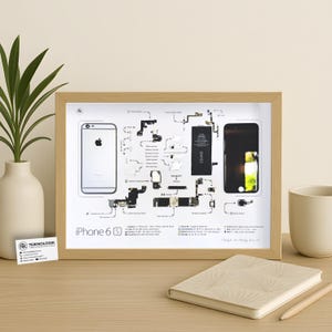 Peut inclure: Un cadre en bois clair contenant une impression schématique de l'iPhone 6S, avec des illustrations de ses composants internes et le texte "iPhone 6S". On peut voir une image du téléphone et un diagramme de ses pièces.