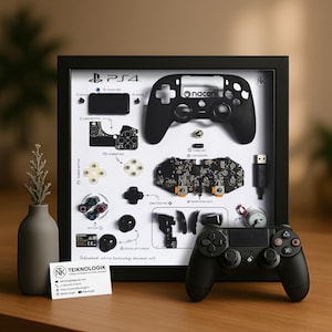 May include: A framed black PS4 controller deconstructed to show its components, including the motherboard, buttons, and a USB cable. A complete black controller sits in front of the frame. The frame includes the text "PS4" and "nacon".