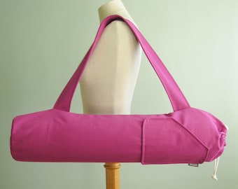 May include: A pink canvas yoga mat bag with a zippered pocket and a drawstring closure. The bag has a long strap for carrying over the shoulder.