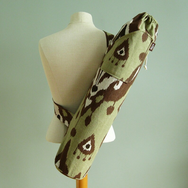 May include: A green and brown yoga mat carrier with a drawstring closure and a pocket on the front. The carrier has a geometric pattern and the word "ETIKA" is printed on the side.