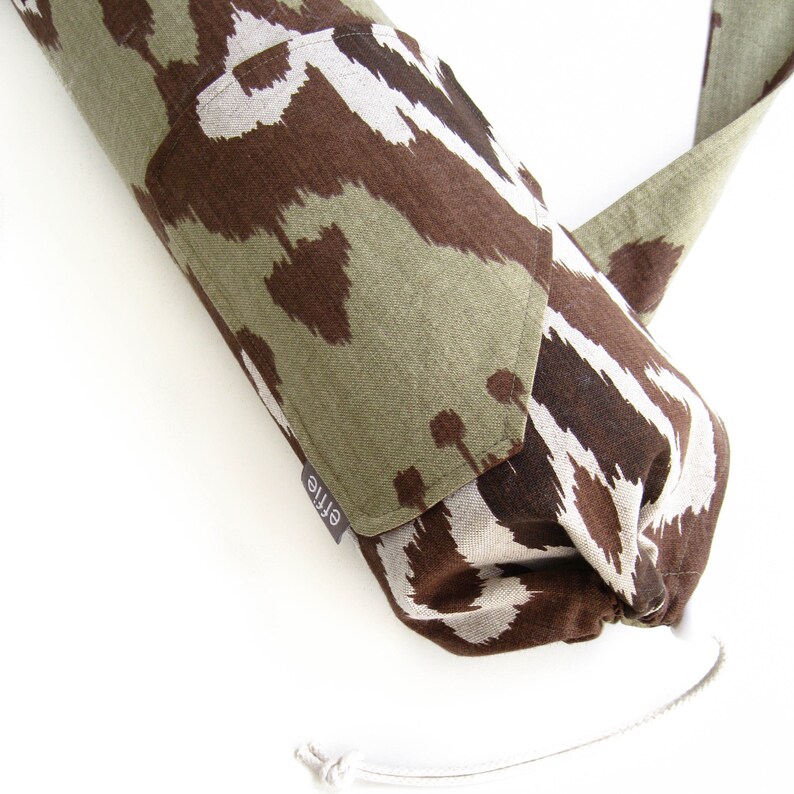 May include: A green and brown patterned yoga mat carrier with a drawstring closure and a small pocket with the word "Ettie" printed on it.