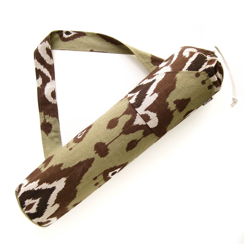 May include: A green and brown patterned yoga mat carrier with a long strap. The carrier has a drawstring closure and the word "STILO" is printed on the side.