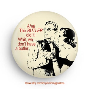May include: A white button with a black and white illustration of a man and woman. The text on the button reads "Aha! The BUTLER did it! Wait, we don't have a butler."