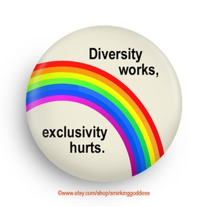 May include: A round, off-white button with a rainbow arc and the text "Diversity works, exclusivity hurts." The rainbow features red, orange, yellow, green, blue, and purple. The button has a slight shadow, suggesting a 3D effect.