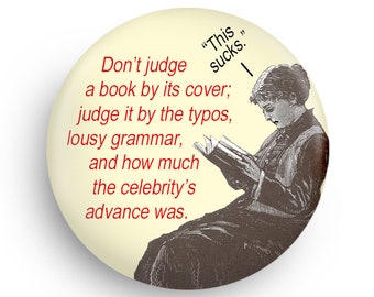 May include: A round button with a cream background and a black and white illustration of a person reading a book. The text on the button reads "Don't judge a book by its cover; judge it by the typos, lousy grammar, and how much the celebrity's advance was."  The text "This sucks." is written in red above the illustration.