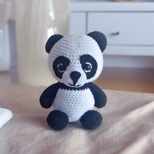 May include: A small crocheted panda bear toy with black and white fur. The panda has black eyes and a black nose.