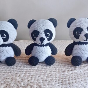 May include: Three crocheted panda bears, each with black eyes, a black nose, and black ears. The pandas are sitting on a white crocheted surface.
