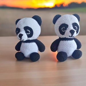 May include: Two crocheted panda bears, one white with black markings and the other black with white markings, sitting on a wooden surface.