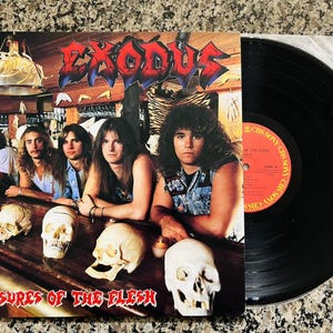 May include: A vinyl record and album cover for the band Exodus. The album cover features the band members at a bar with skulls. The album title "Pleasures of the Flesh" is at the bottom. The vinyl record is black.