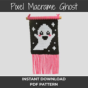 May include: A macrame wall hanging with a pixelated ghost design. The ghost is white against a black background with white crosses. The top is wrapped in pink yarn, and the bottom has pink fringe. Text at the top reads "Pixel Macrame Ghost".