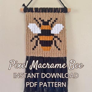 Pode incluir: Uma tapeçaria de macramé com um design de abelha pixelizada em preto, amarelo e branco sobre um fundo castanho claro, suspensa num pau de madeira com um cordão preto. O texto diz: Pixel Macrame Bee INSTANT DOWNLOAD PDF PATTERN.