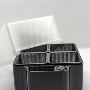 May include: A black 3D printed box with four compartments and a lid. The lid is translucent white and has a textured surface.