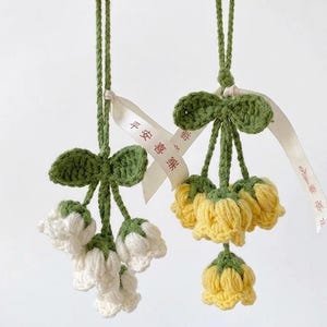 May include: Two handmade crochet flower ornaments. One features white flowers, the other yellow. Both have green leaves and stems, with a green bow at the top. Each ornament has a white ribbon with Chinese characters.