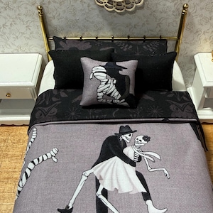 Peut inclure: Un lit de maison de poupée miniature avec une couverture grise ornée d'un motif de deux squelettes dansants en tenue de soirée. La literie comprend deux oreillers noirs unis et un coussin carré représentant une momie sur fond sombre.