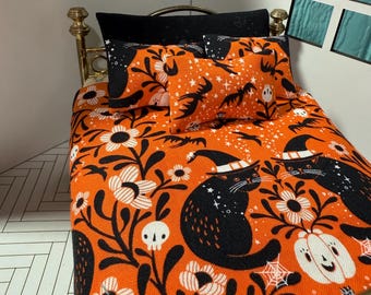 May include: Miniature Halloween-themed bed set with an orange and black color scheme. The bedding features a repeating pattern of black cats wearing witch hats, white flowers, skulls, and pumpkins. Includes a gold-colored bed frame.