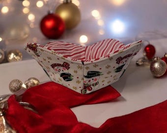 May include: A white fabric bowl with a red and white striped lining. The bowl is decorated with a snowman pattern and gold snowflakes. The bowl is sitting on a red and white fabric surface.