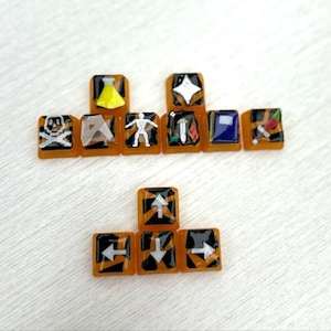 May include: A collection of square, orange-toned resin tiles with various white and black symbols. The symbols include a skull and crossbones, a flask, a star, a person, a book, and arrows. The tiles are arranged in a grid-like pattern.