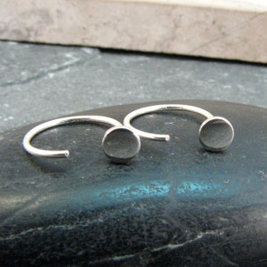 Può includere: Un paio di orecchini a cerchio d'argento con un disco rotondo all'estremità di ogni cerchio.