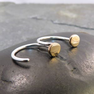 May include: A pair of silver hoop earrings with gold-toned round accents. The earrings are simple and elegant.