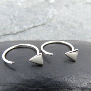 May include: A pair of silver triangle hoop earrings. The earrings are made of a thin wire and have a small triangle charm at the end.