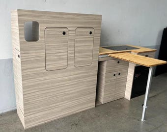 May include: A light wood-toned cabinet with two doors and a small window. The cabinet is attached to a countertop with a fold-down table. The table is made of light wood and has a white metal support.