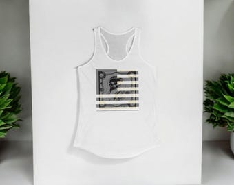 May include: White racerback tank top with a graphic design. The design features a black and white image of a person with horizontal stripes. The tank top is displayed against a white background with green plants on either side.