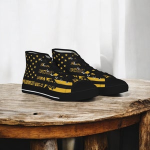 May include: Pair of high-top sneakers with a black base and a striking design. The design features a gold star pattern on the upper, complemented by gold and black decorative elements. The shoes have black soles and a white stripe.